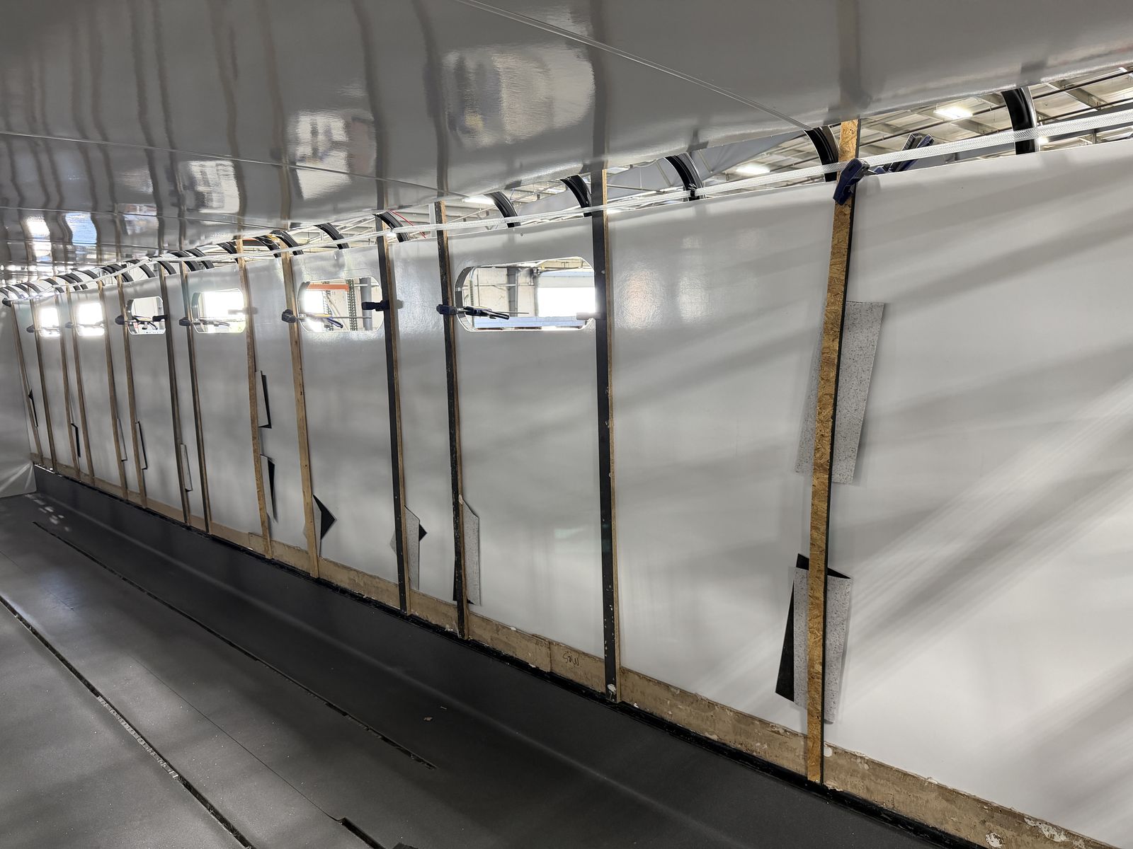 One-piece sidewall panel being pressure-laminated onto the steel cage, held with wood strips and clamps